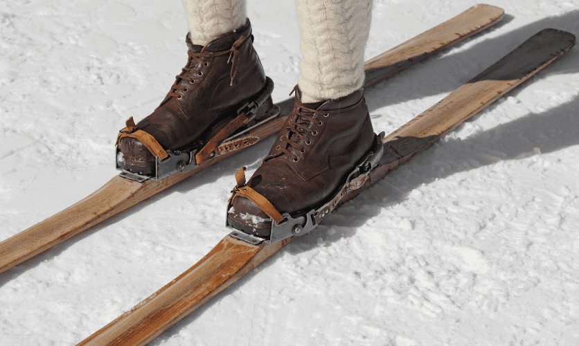 The history of ski bindings: an image showing traditional early wooden with a simple leather strap binding across the toe of a lace up leather boot