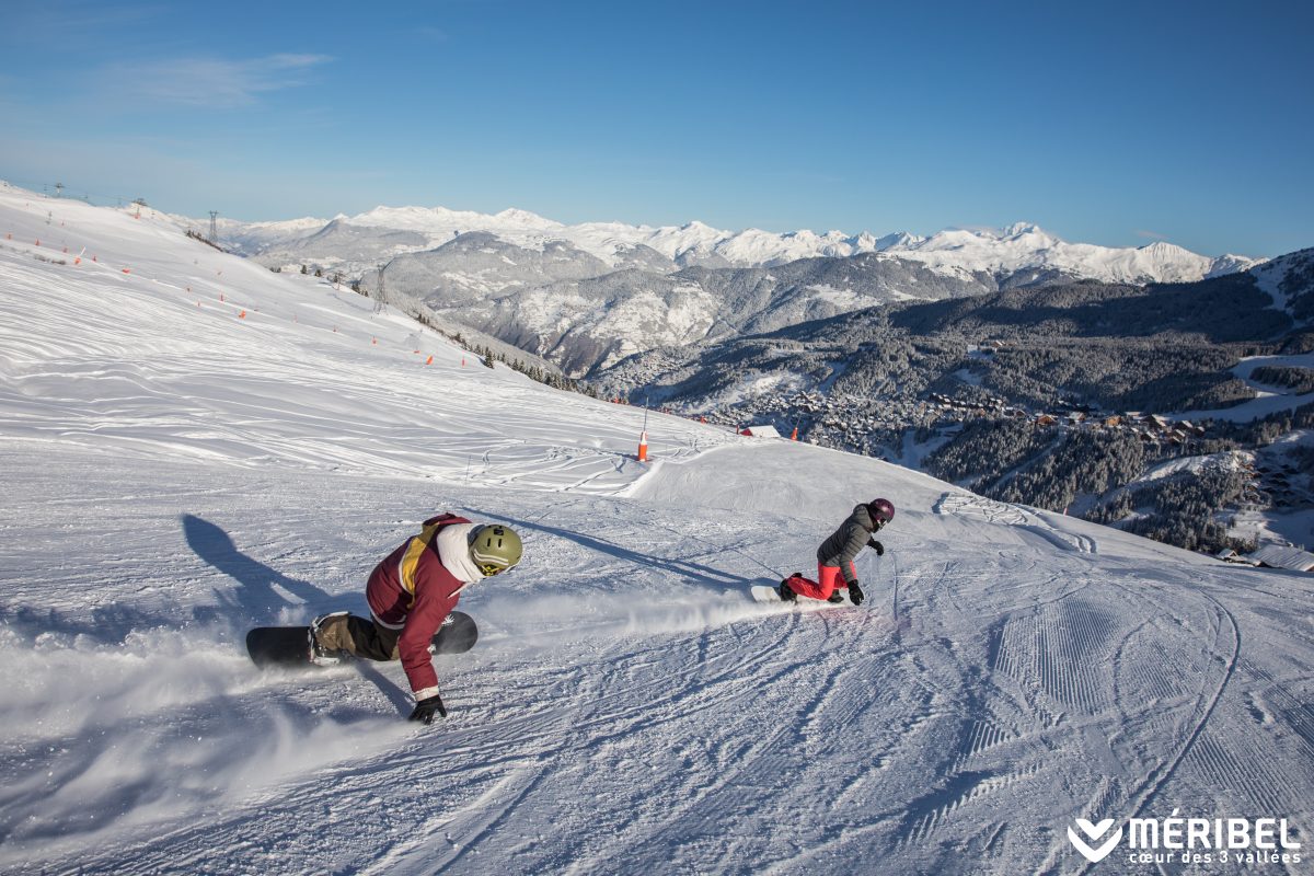 Two people snowboarding down a run in Meribel. 
