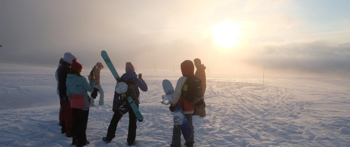 Friends in the snow with snowboards and sunset