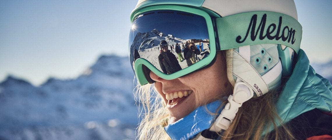 Woman skiing with helmet and reflection of friend in goggles